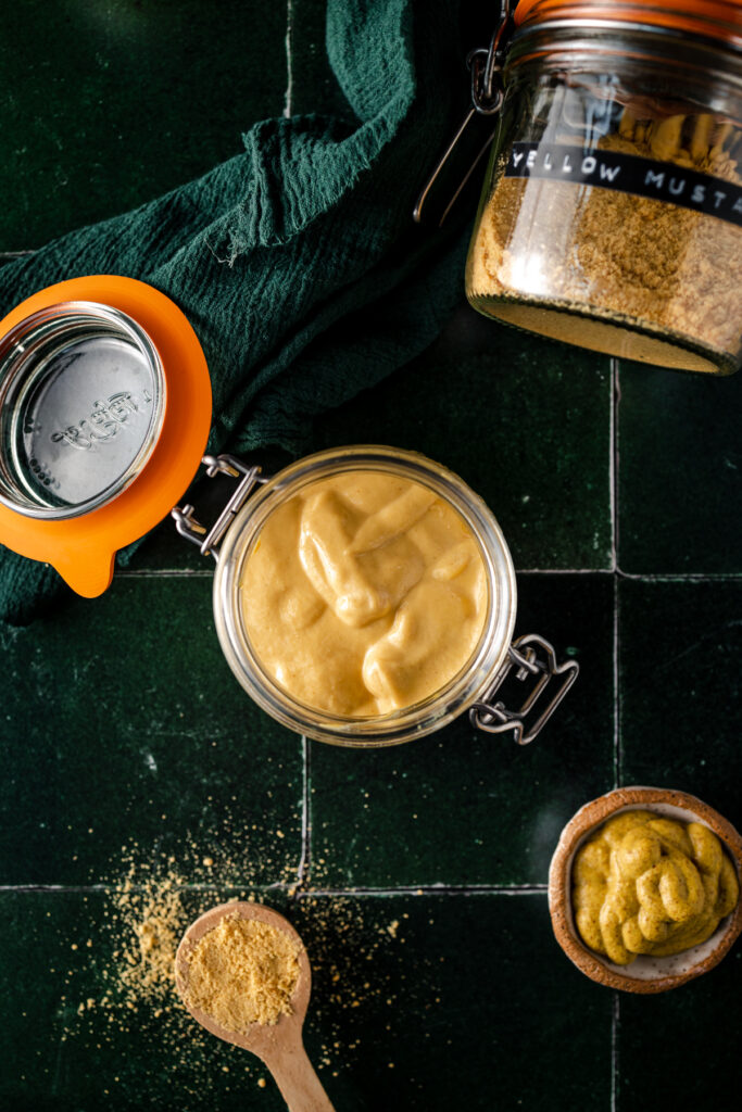 A jar of mustard and a spoon on a tiled table.
