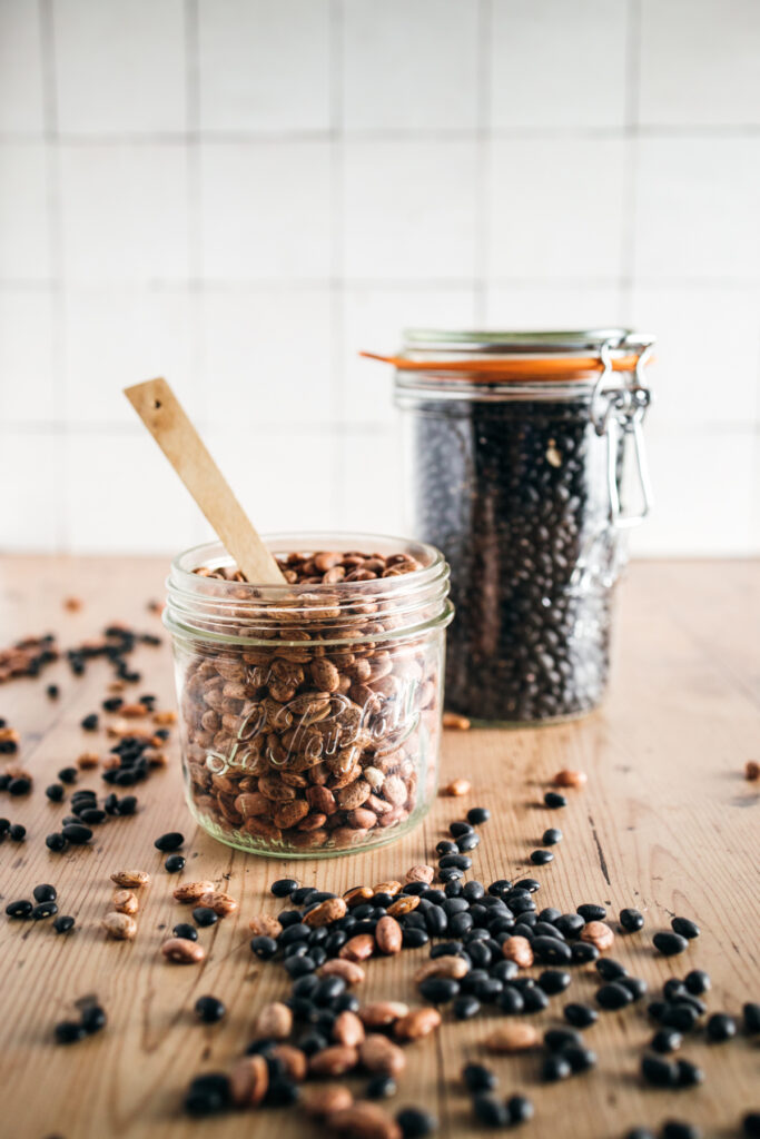 Black beans and pinto beans in jars on a wooden table.