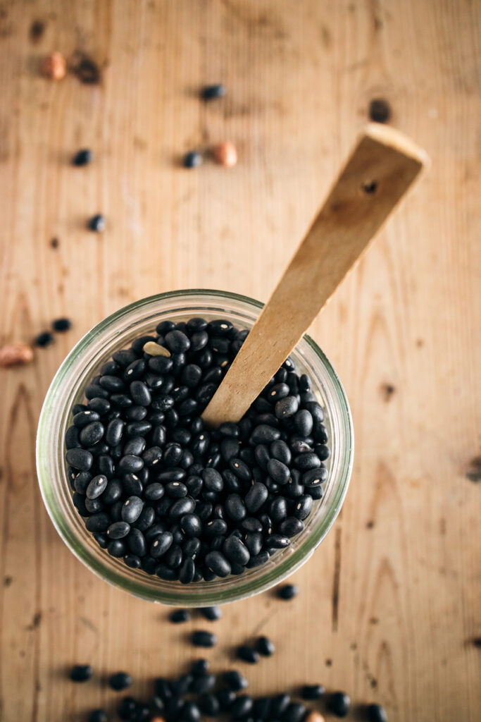 Black beans in a glass bowl with a wooden spoon.