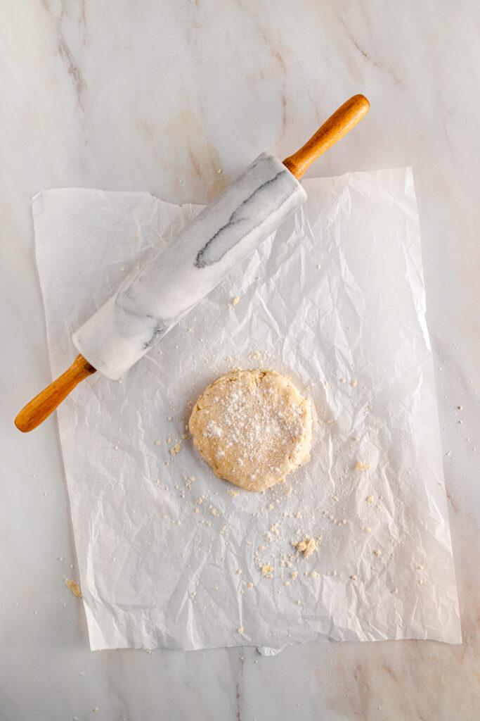 A doughnut on a parchment paper next to a rolling pin.