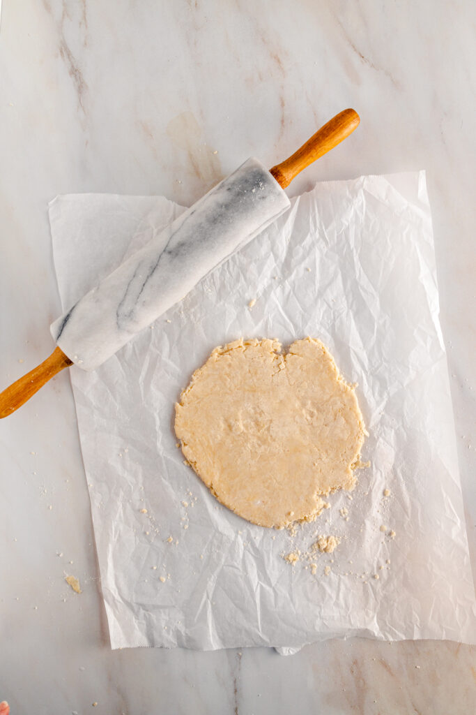 A piece of dough and a rolling pin on a piece of paper.