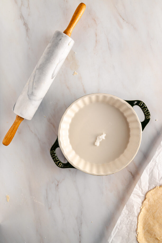 A bowl of dough and a rolling pin on a marble countertop.