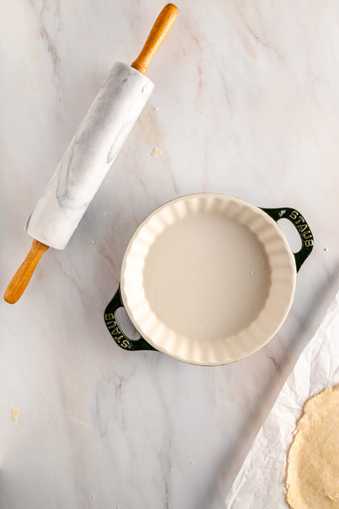 A pie crust and a rolling pin on a marble table.