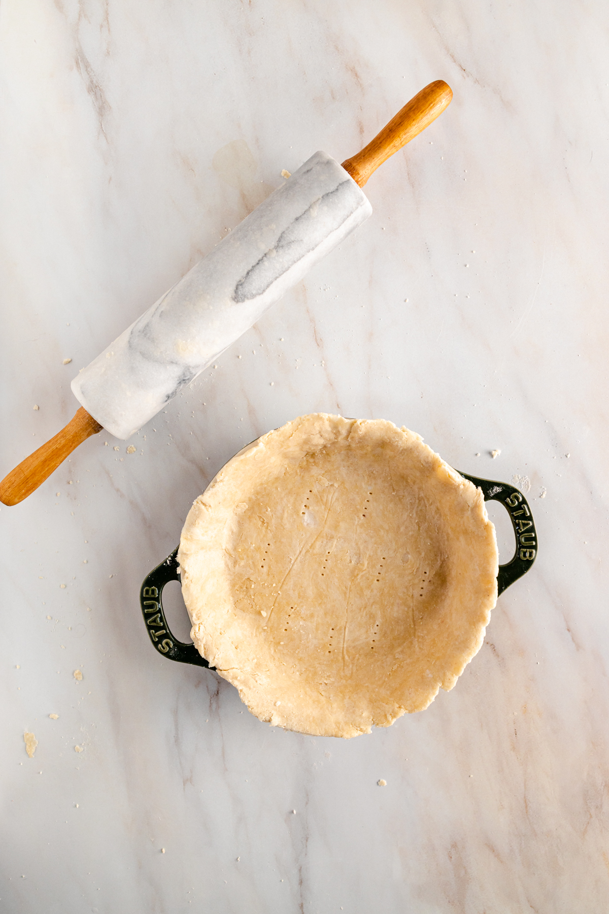 A pie crust and a rolling pin on a marble countertop.