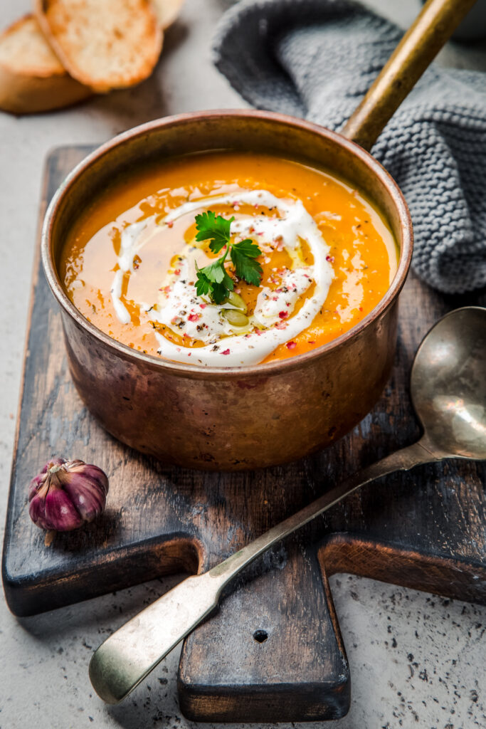 Tasty dairy-free pumpkin soup in a copper pan on top of a wooden cutting board.