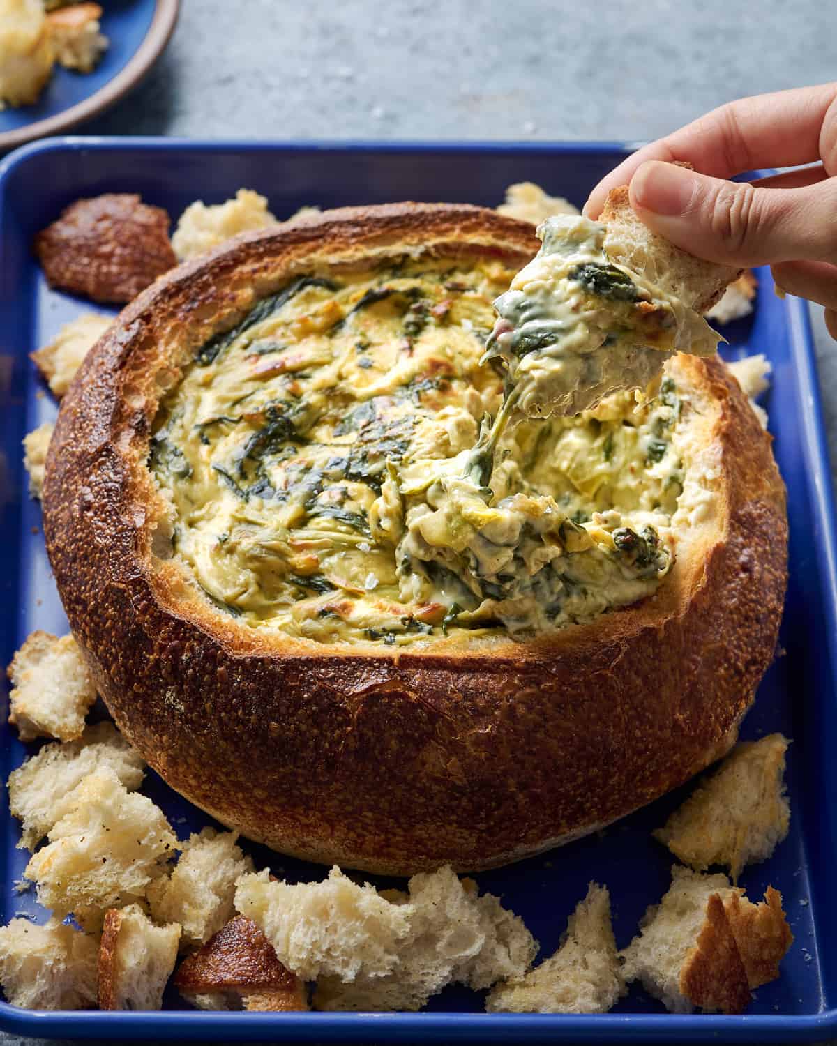 A person is dipping bread into a bowl of spinach dip.