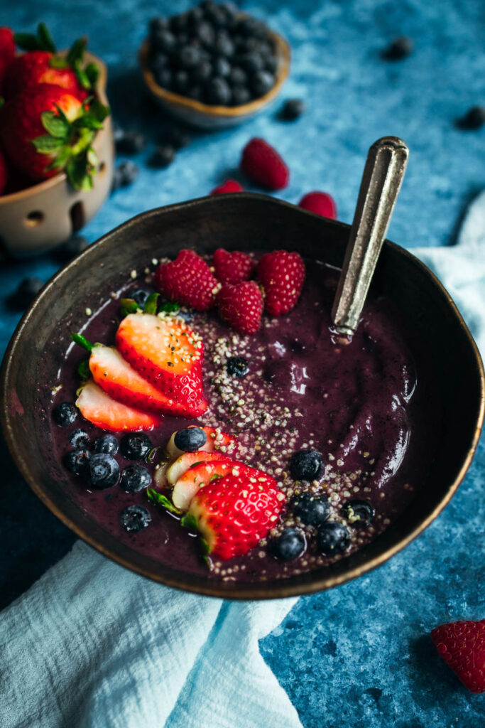 A bowl of blueberry smoothie with berries and chia seeds.