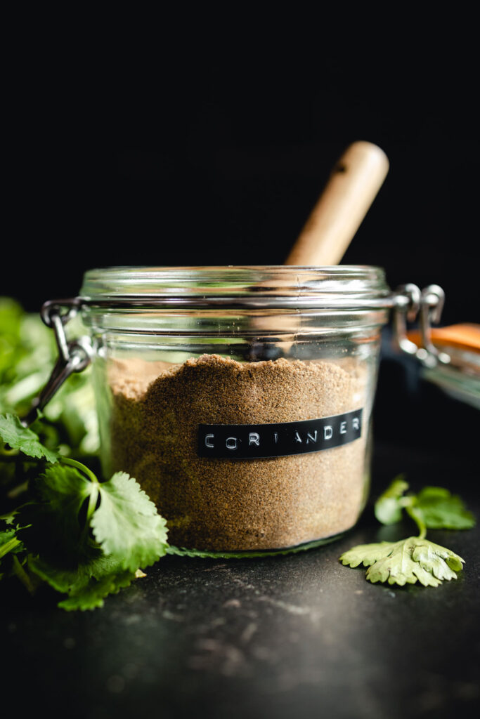 Coriander powder, a substitute for cilantro, in a glass jar with a wooden spoon.