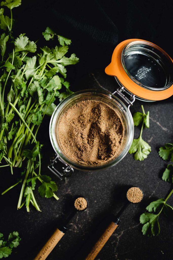 Coriander powder, a substitute for cilantro, in a bowl on a black table.