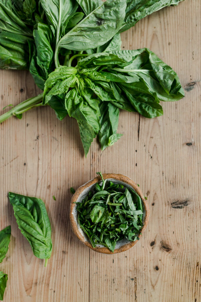 Fresh basil leaves in a bowl on a wooden table.