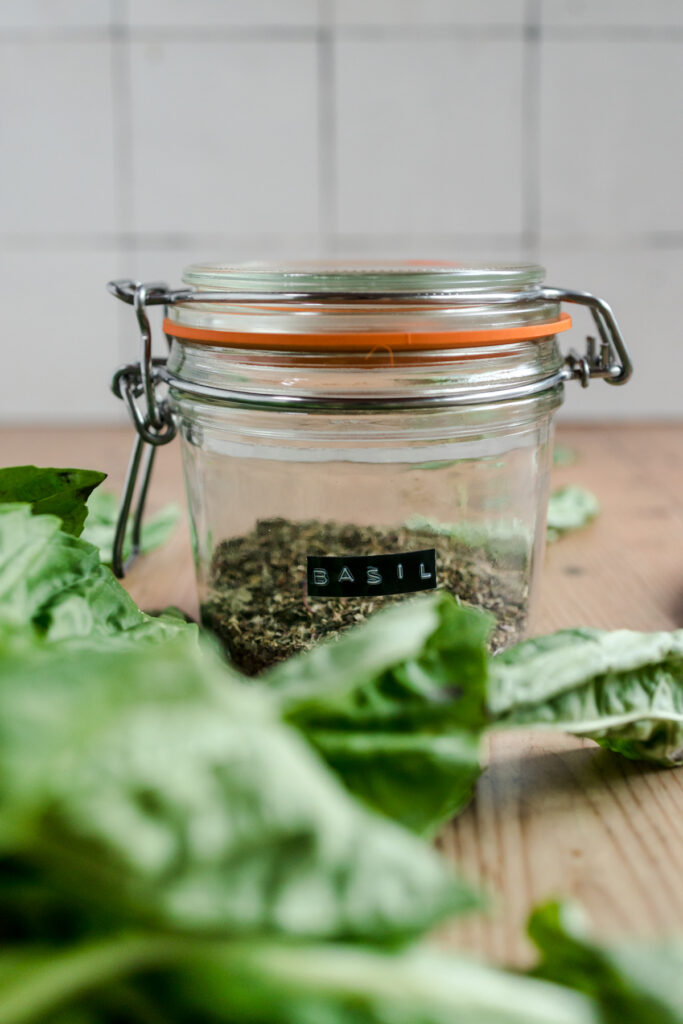 A glass jar filled with basil leaves on a wooden table.