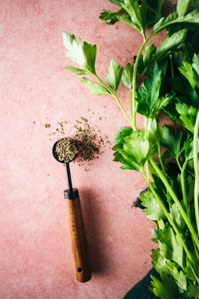 Fresh parsley and a wooden spoon on a pink background.