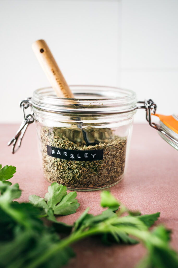 A glass jar with herbs and a wooden spoon.