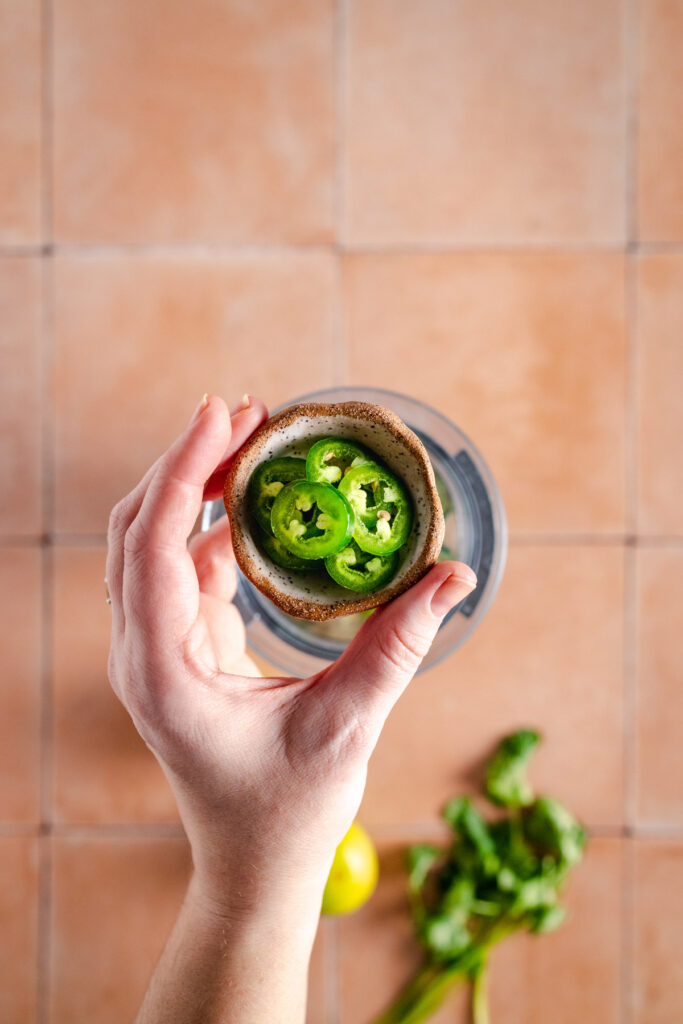 A hand holding a bowl of green peppers.