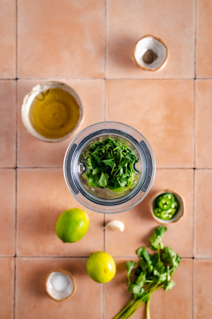 A blender filled with herbs and lemons on a tiled floor.