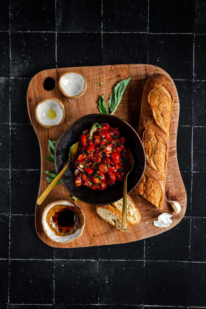 A bowl of tomato sauce and bread on a wooden cutting board.