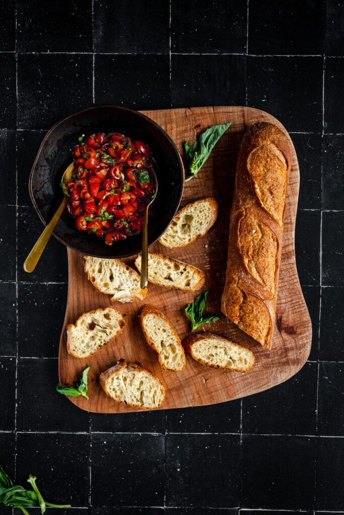 A bowl of tomato sauce and bread on a wooden cutting board.
