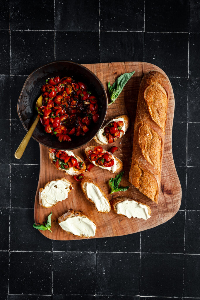 A wooden cutting board with bread and tomato sauce.