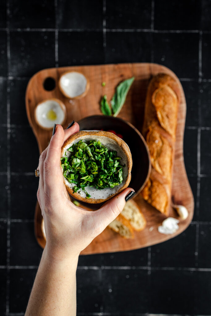 A hand holding a bowl of basil on a wooden cutting board.