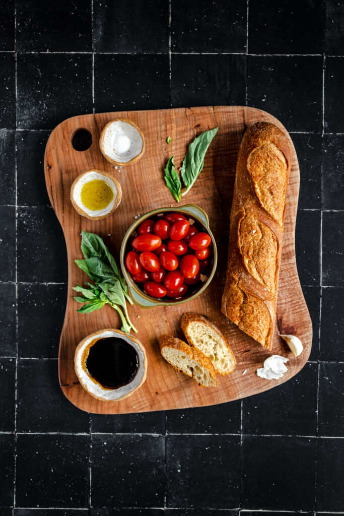 A wooden cutting board with bread, tomatoes and basil.