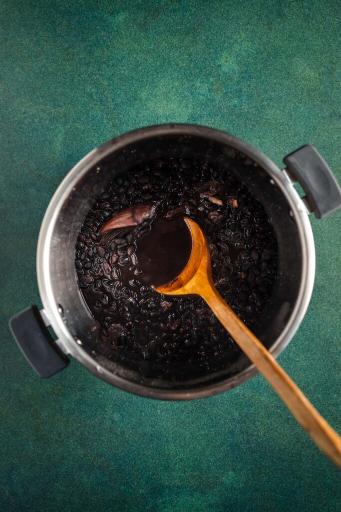 A pot with a wooden spoon filled with black beans.