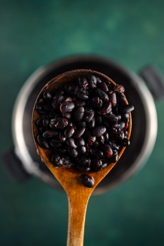 Black beans in a wooden spoon on a green background.