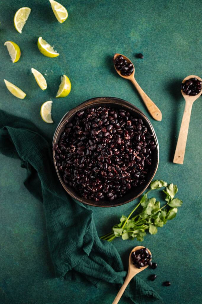 Black beans in a bowl with lime and cilantro on a green background.