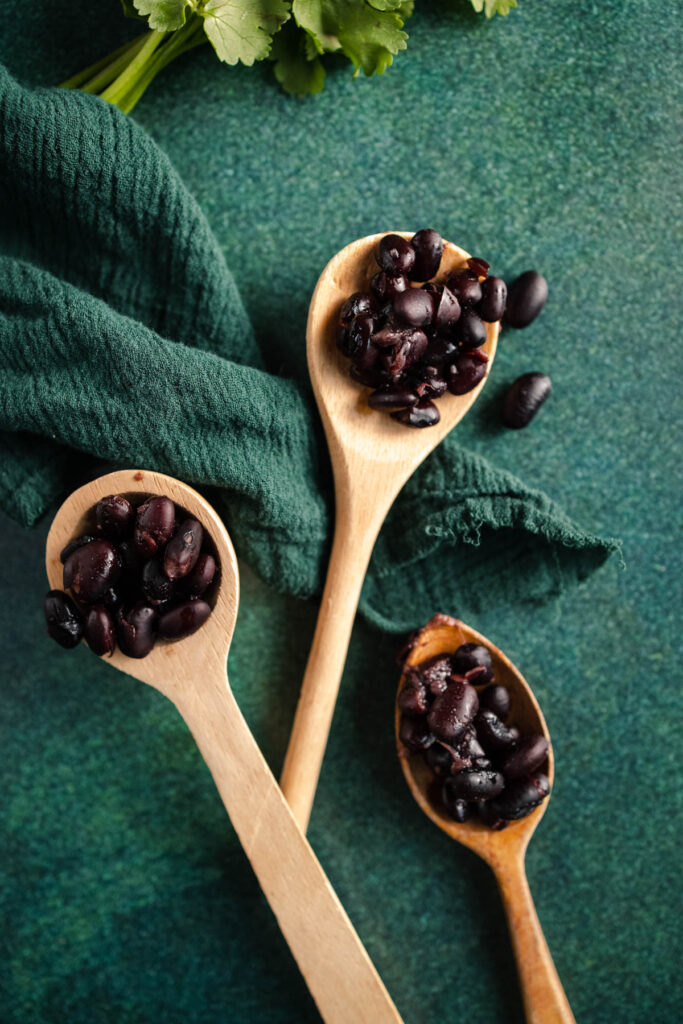 Black beans in wooden spoons on a green background.