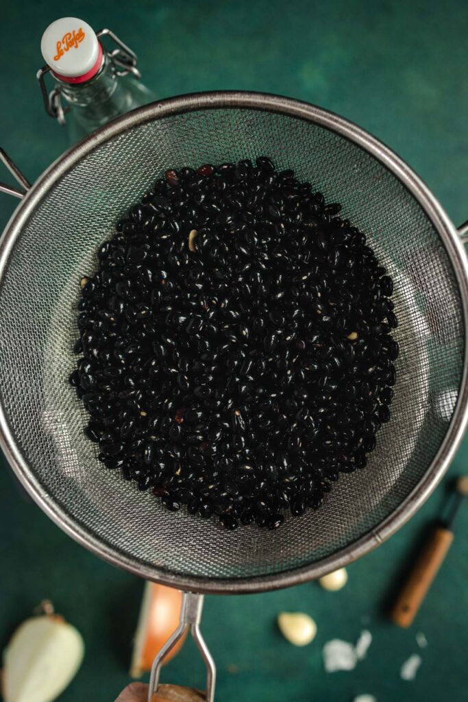 Black beans in a strainer on a green table.