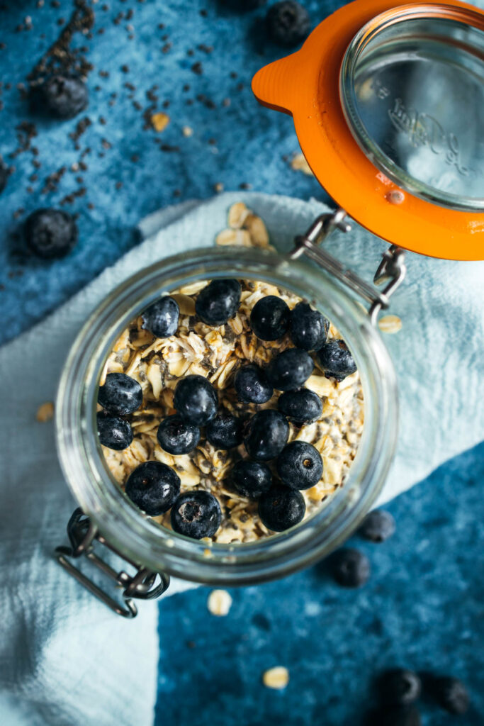 Blueberries and oats in a glass jar on a blue background.