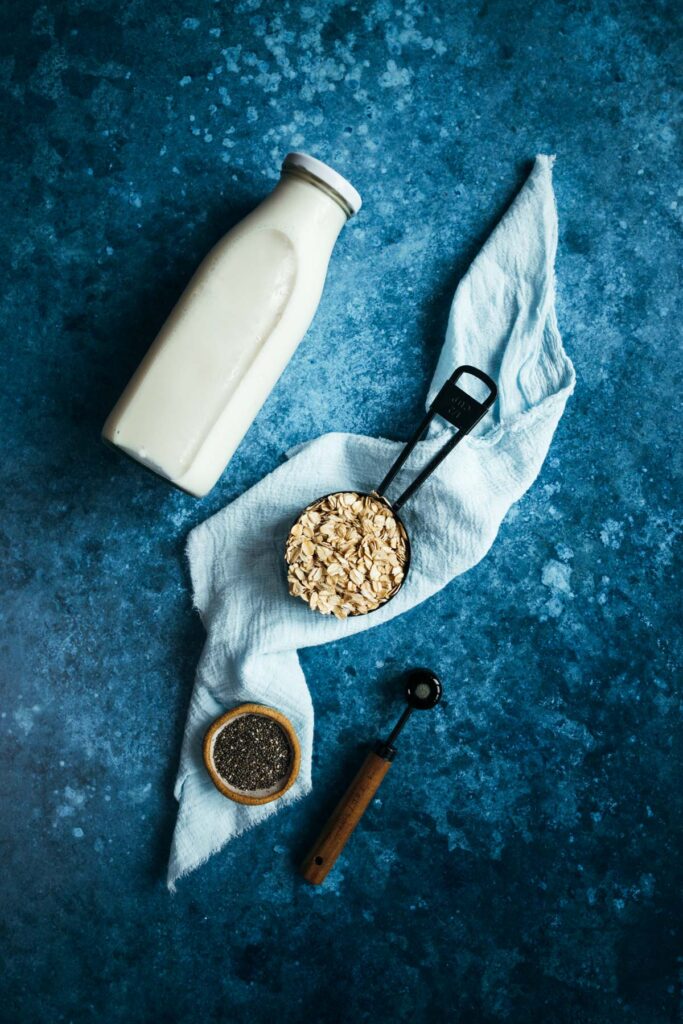 A bottle of milk, oats and a spoon on a blue background.