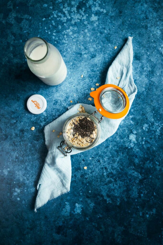 A glass of milk and oats on a blue table.