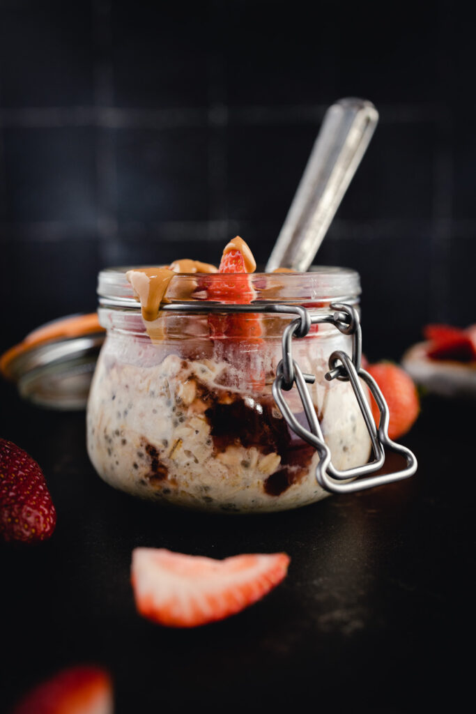 A jar of oatmeal with strawberries and a spoon.