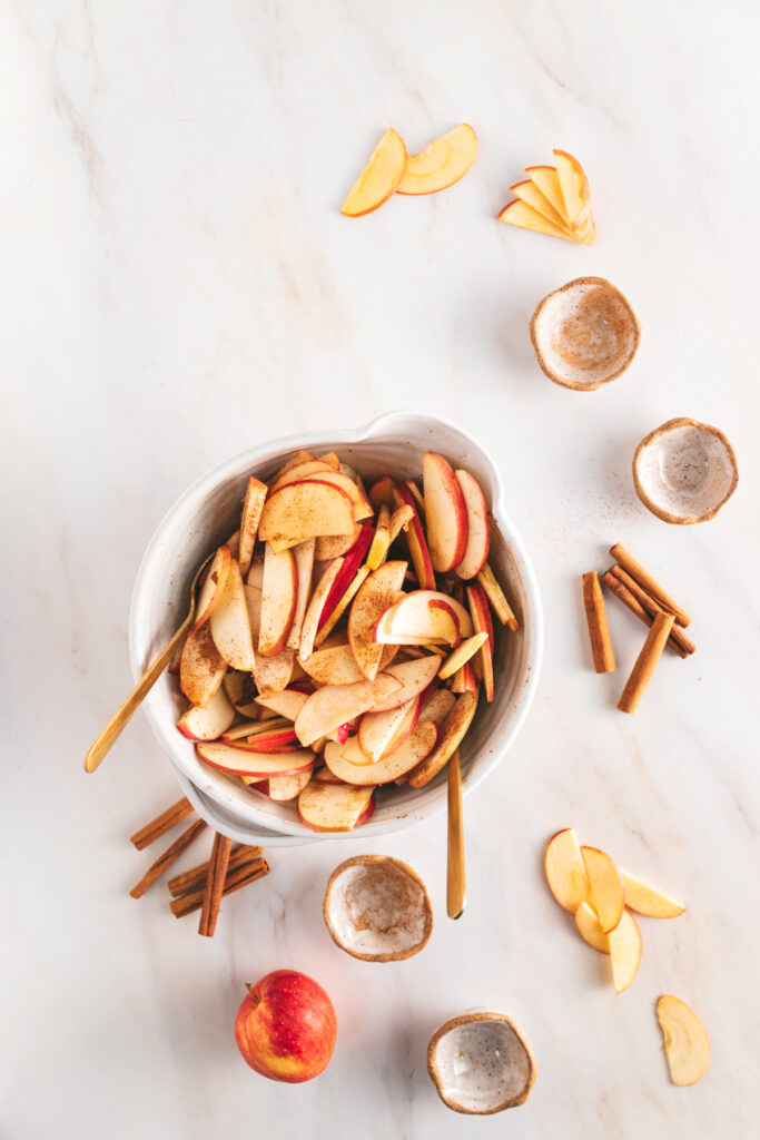 Sliced apples and spices in a bowl on a marble table.
