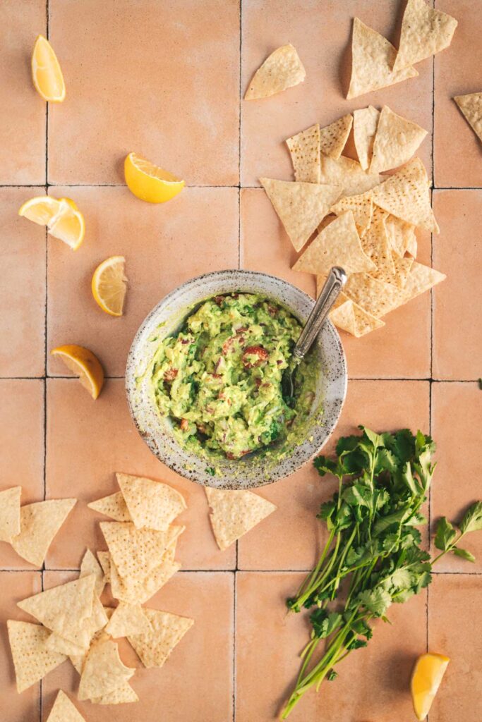 A bowl of guacamole and tortilla chips on a tiled floor.
