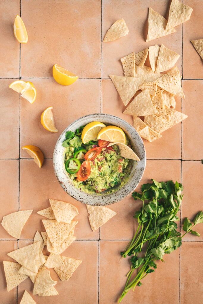 A bowl of guacamole and tortilla chips on a tiled floor.