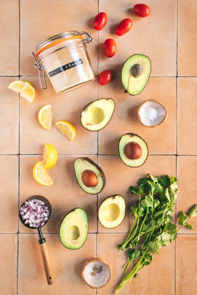 Avocados, tomatoes, lemons, cilantro, and limes on a tiled floor.