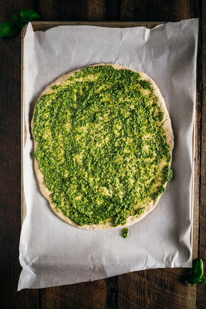 A pizza with pesto on a baking sheet.