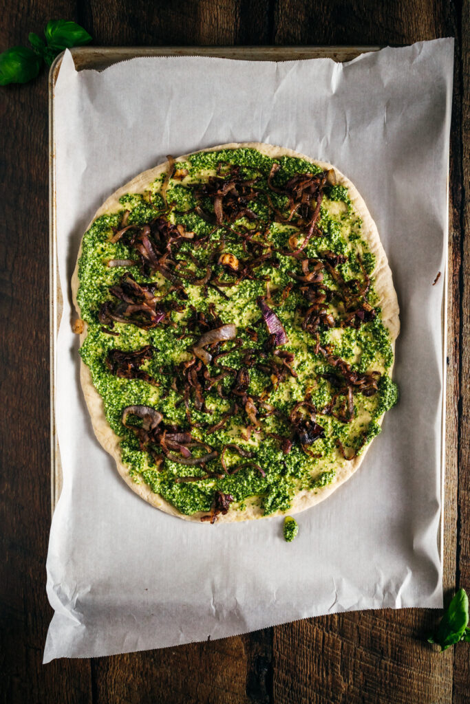 A pizza with pesto on top of a sheet of paper.