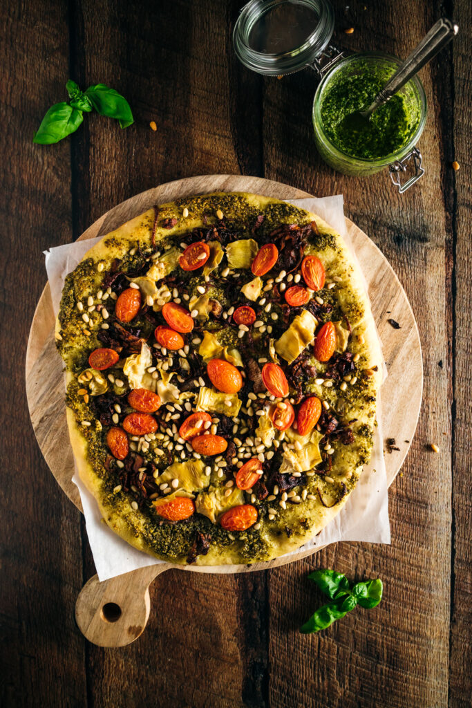 A pizza with pesto and tomatoes on a wooden board.