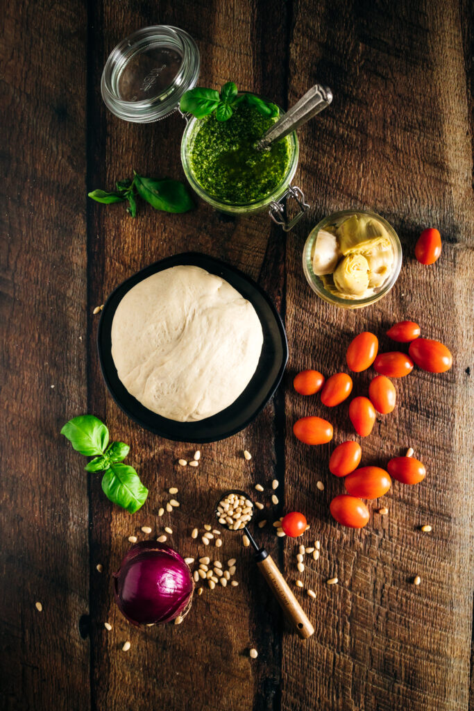 A pizza dough, tomatoes, herbs and spices on a wooden table.