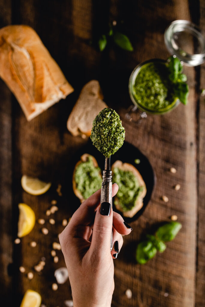 A person holding a spoon with pesto on it.