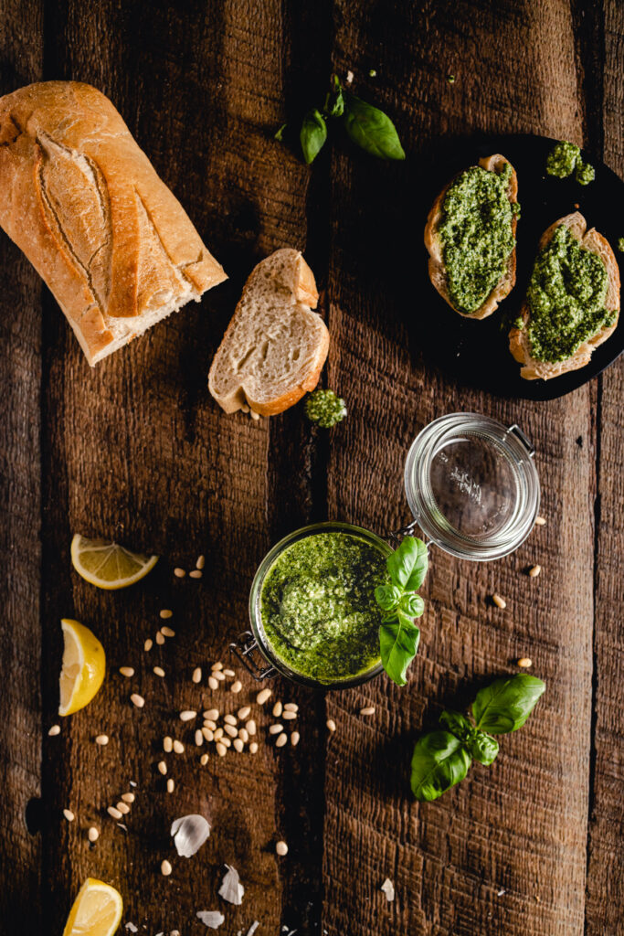 A bowl of pesto, bread and lemons on a wooden table.