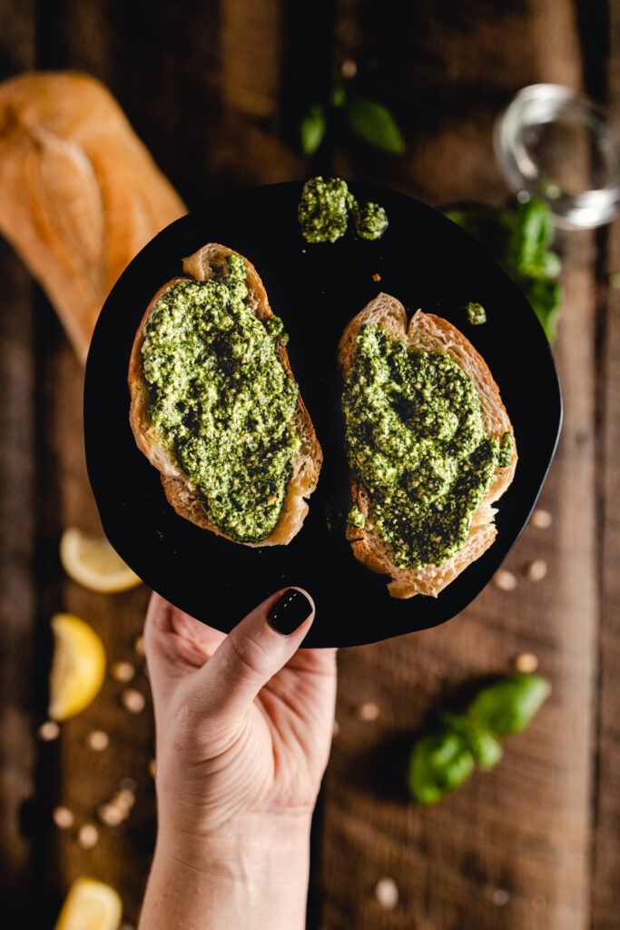 A person holding a bread with pesto on it.