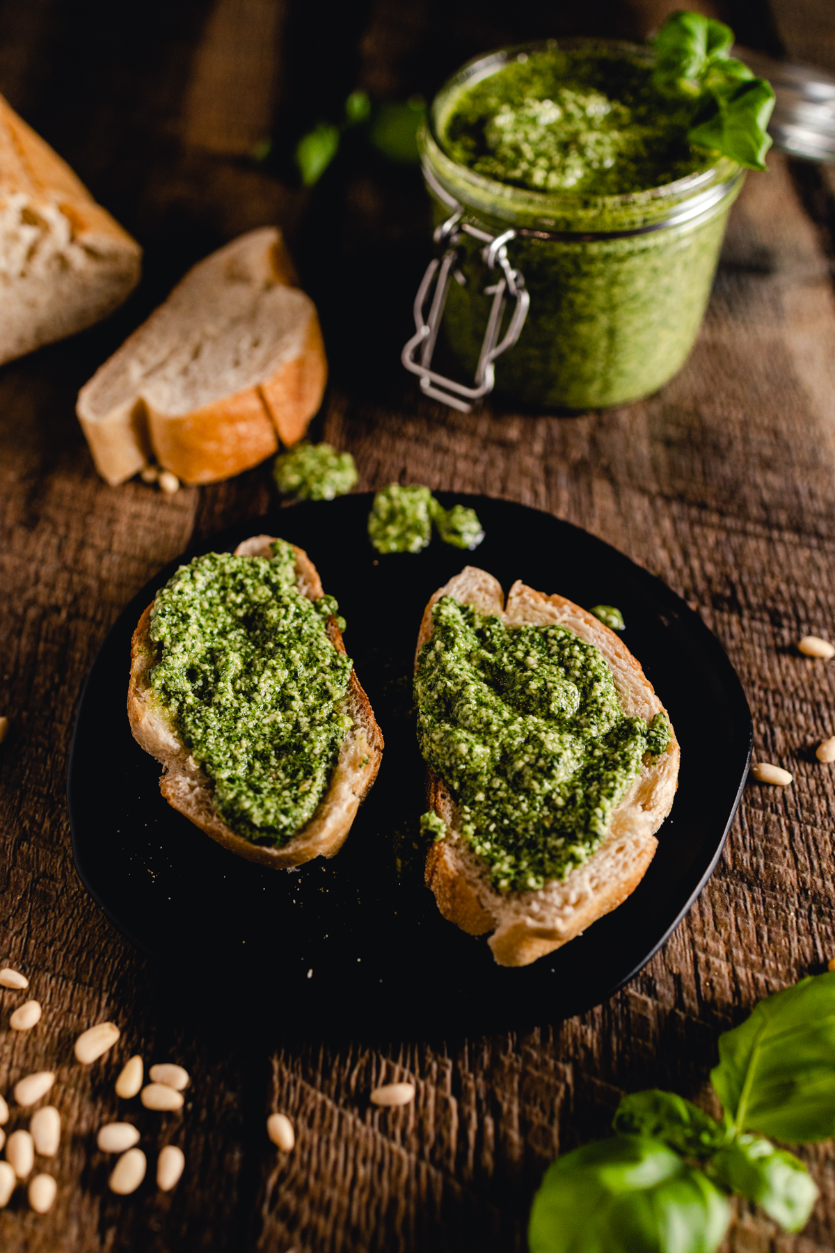 Pesto pesto on toasted bread with a jar of pesto on a wooden table.