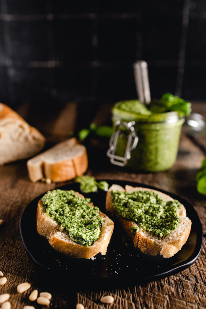 Two slices of bread with pesto sauce on a black plate.