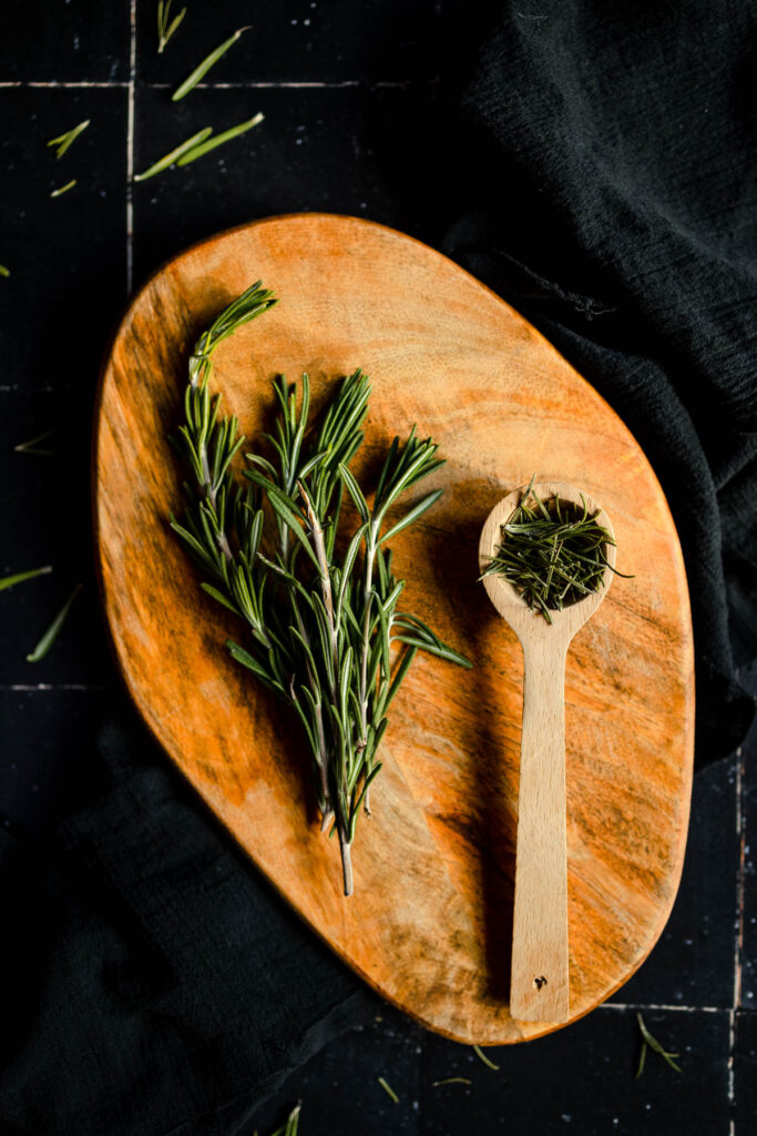 Rosemary sprigs and a wooden spoon on a wooden board.