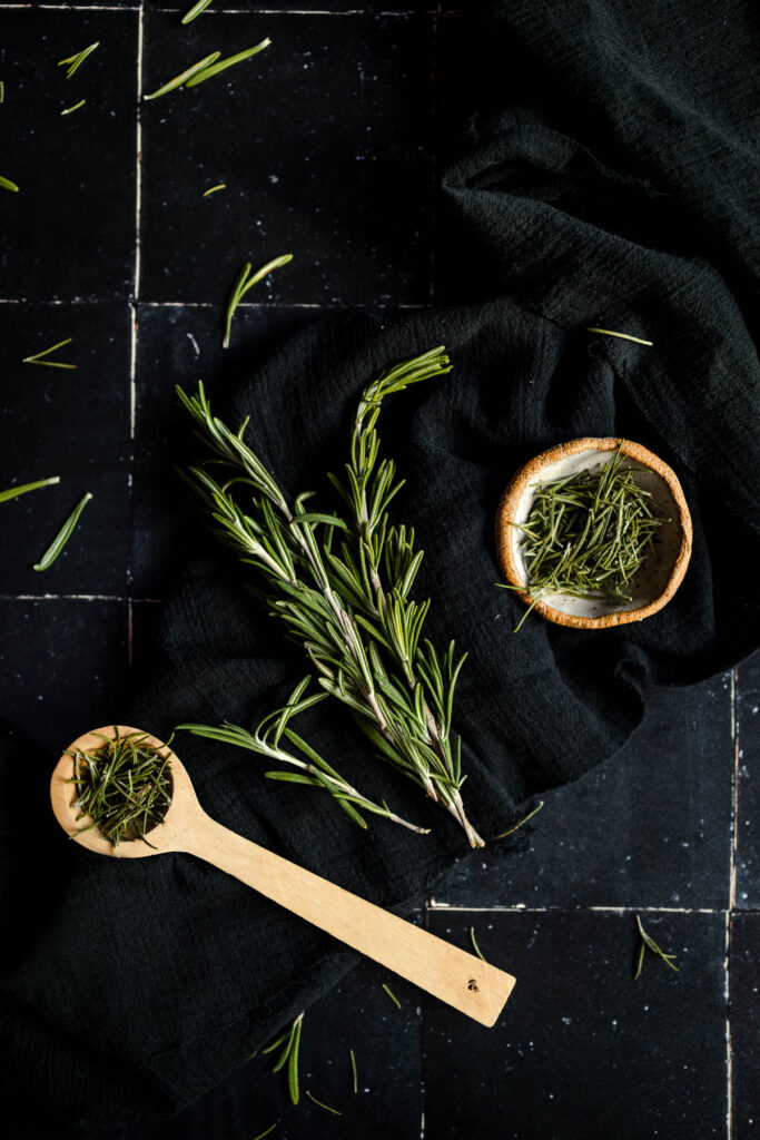Sprigs of rosemary and a wooden spoon on a black background.