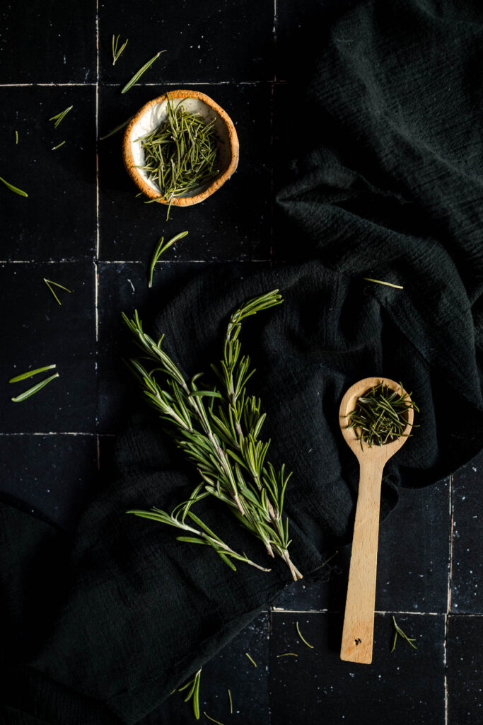 Rosemary sprigs and a wooden spoon on a black background.