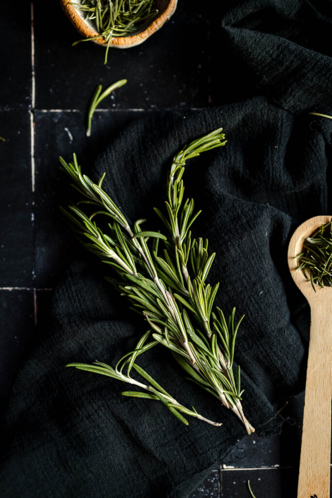 Rosemary leaves and a wooden spoon on a black table.